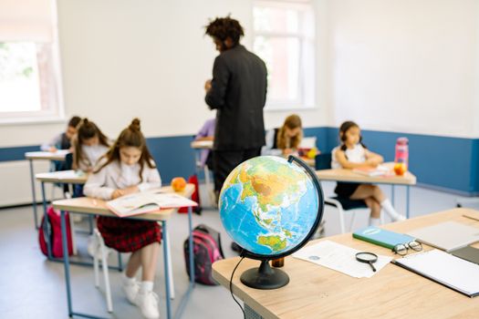 A classroom scene with students studying geography, highlighted by a prominent globe on the teacher's desk.