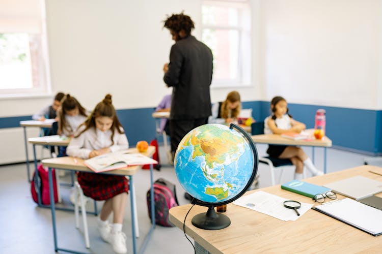 A Desk Globe On A Wooden Desk In A Classroom