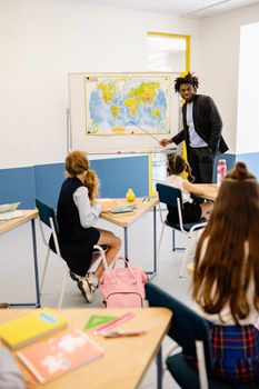 Teacher engaging students with a world map during a classroom geography lesson.