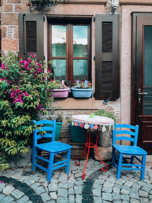 Round table with blue wooden chairs on paved street near house with plants on daytime
