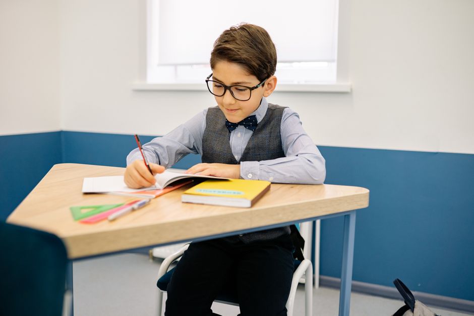 Photo by Yan Krukau on Pexels A young boy with glasses sits at a desk, writing in a notebook in a classroom. - Photo by Yan Krukau on Pexels