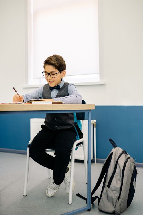 Free Boy in eyeglasses writing in a classroom, showing focused learning and study habits. Stock Photo
