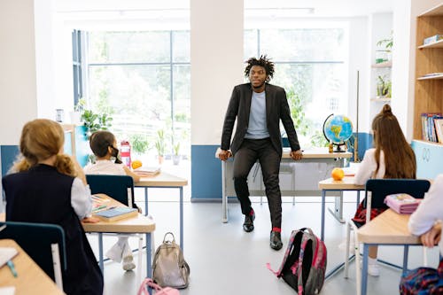 Man in Black Suit Jacket Sitting on a Tablet Inside the Classroom