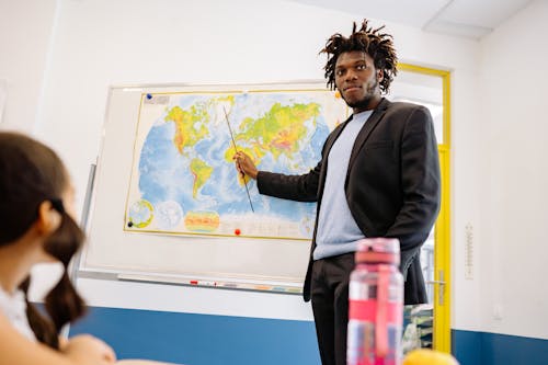 A Man Pointing at a World Map on a Whiteboard in a Classroom