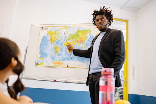 Male teacher using a pointer to describe a world map during a classroom lesson.