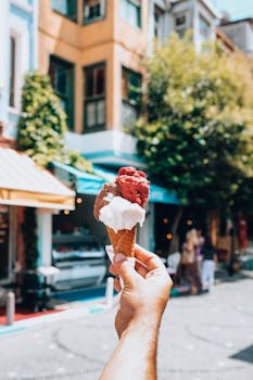 Hand holding a three-flavored ice cream cone on a sunny street background.