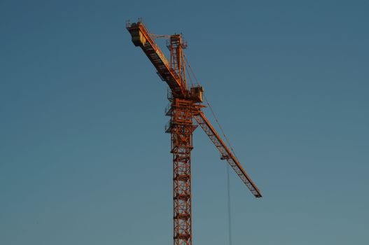 Tower crane silhouetted against a clear blue sky at sunset.