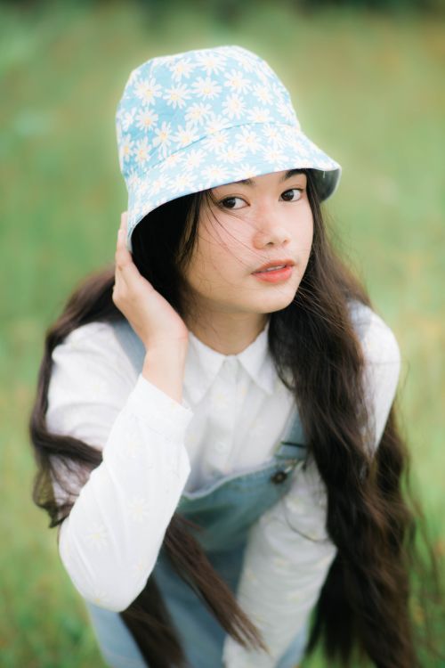 Free Portrait of a woman with long hair wearing a floral bucket hat in a green field. Stock Photo