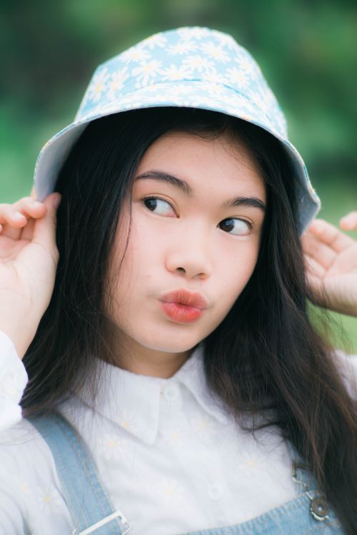 Free Close-up portrait of an Asian woman wearing a bucket hat, playfully posing outdoors. Stock Photo