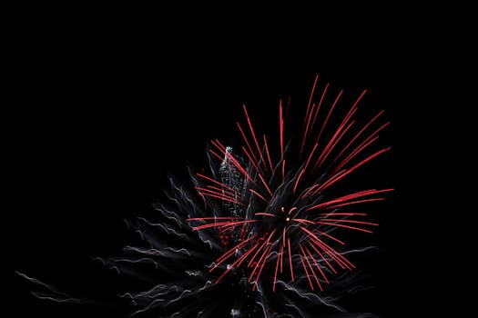 Explosive red fireworks bloom dramatically in the night sky.