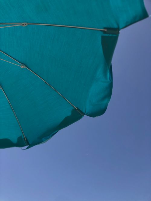 Free A vibrant blue umbrella set against a clear, sunny summer sky. Perfect for vacation themes. Stock Photo