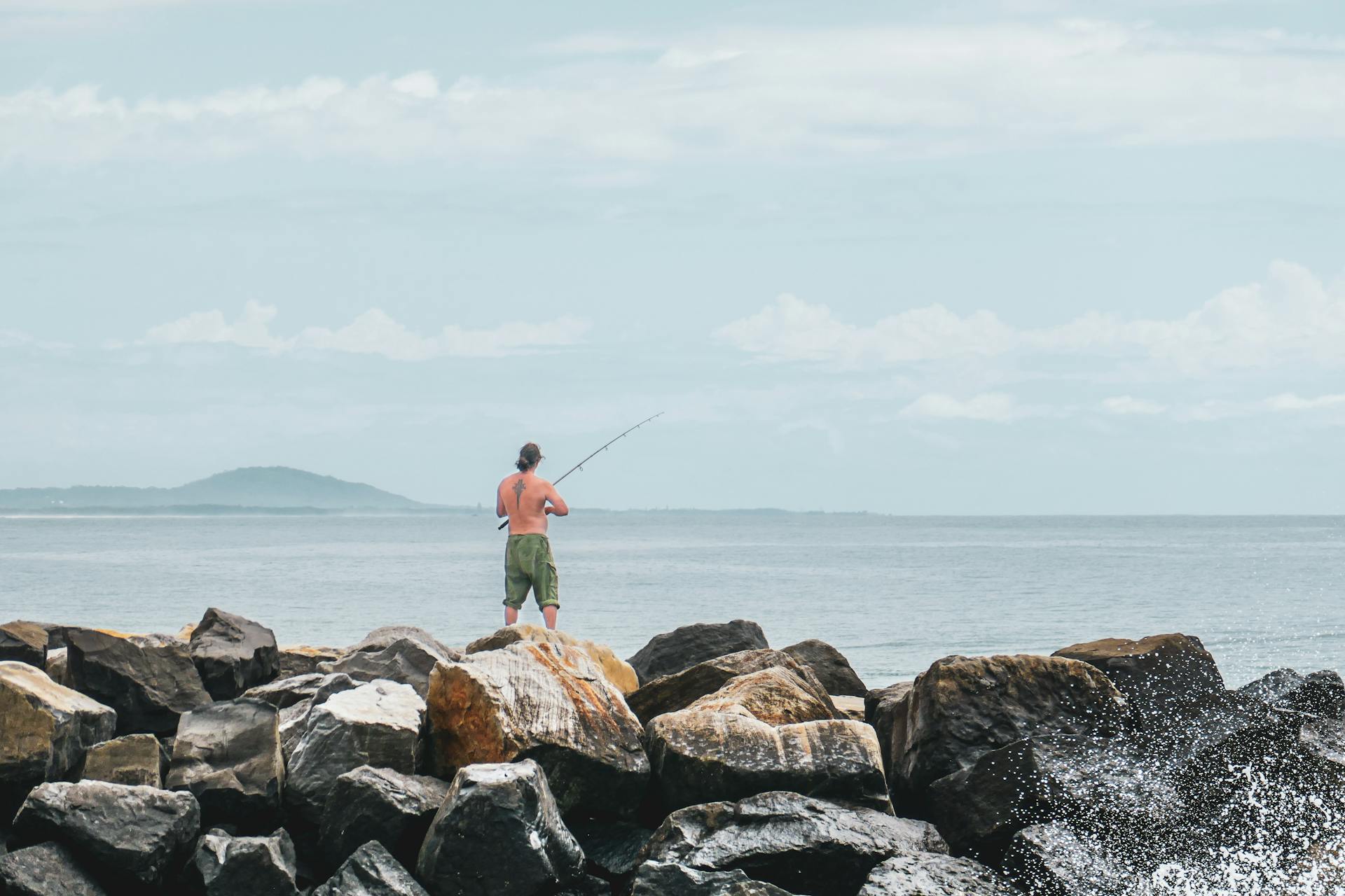 Man fishing shirtless on rocky shore at Brunswick Heads, Australia.