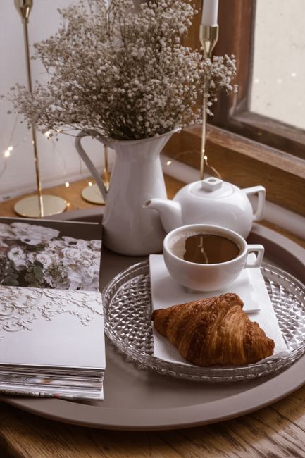 Elegant French breakfast setup with coffee, croissant, and flowers in warm lighting.
