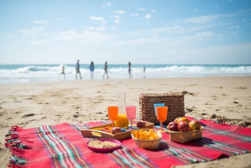 Free A vibrant picnic scene on a Portuguese beach featuring food, drinks, and a view of the ocean. Stock Photo