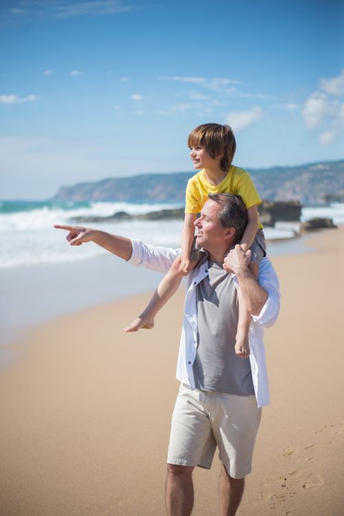 Free Father carrying son on shoulders, enjoying a sunny beach day in Portugal. Stock Photo