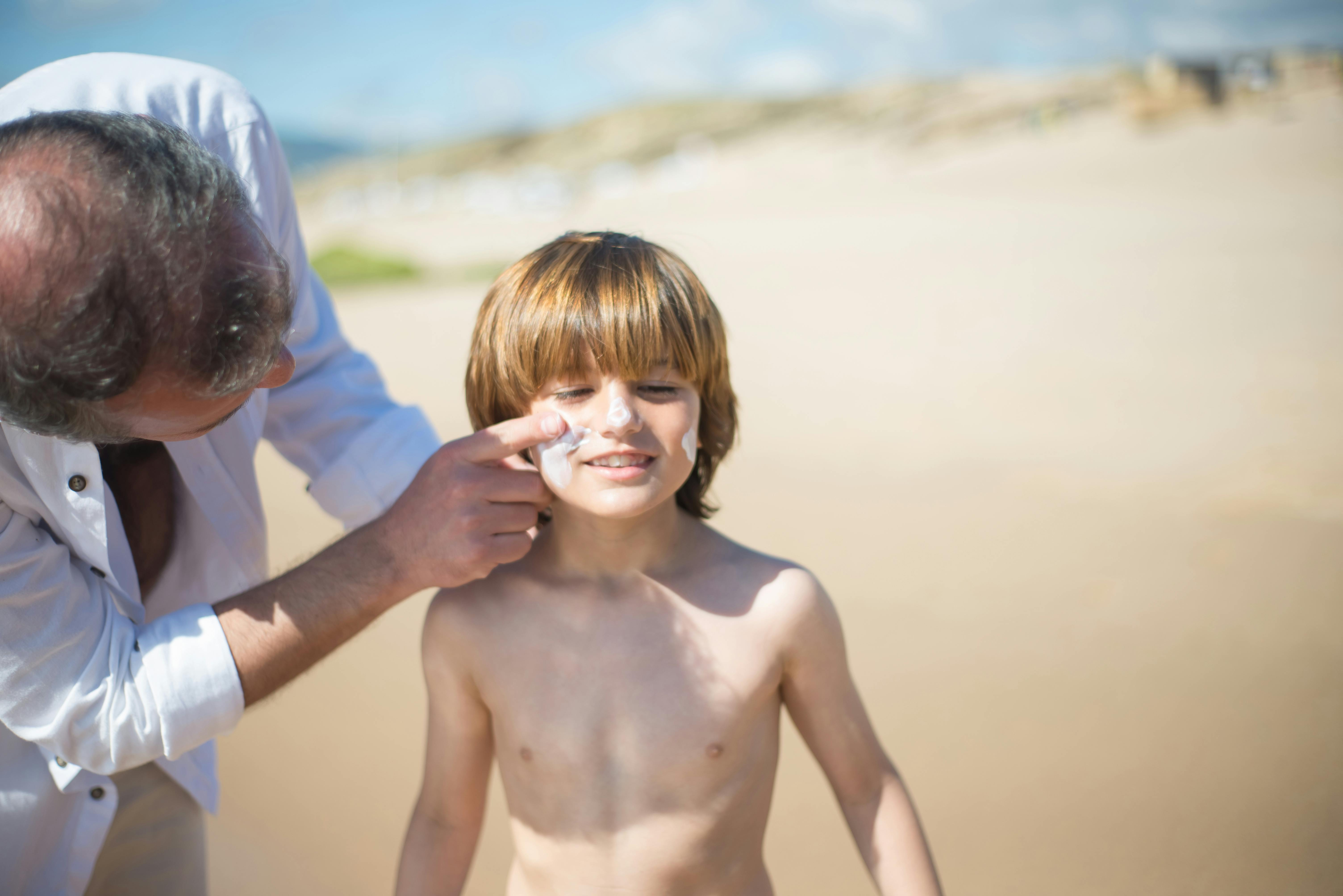 A father applying sunscreen to his son on a sunny Portuguese beach, emphasizing sun safety.