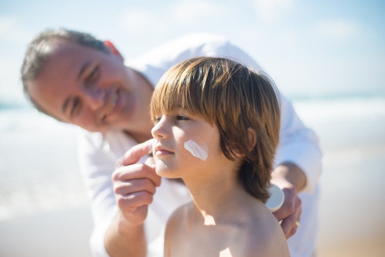 A Man Applying A Sunscreen On His Son's Face