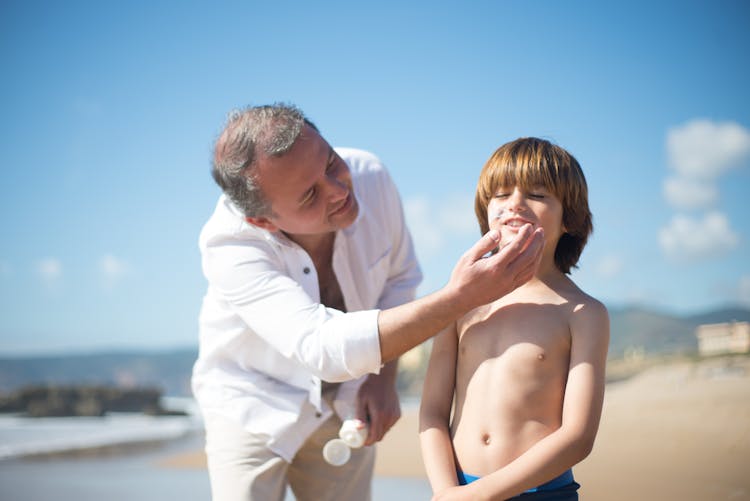 A Man Applying Sunscreen To A Young Boy's Face