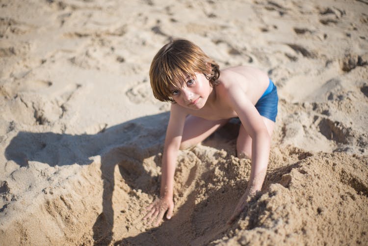 A Shirtless Young Boy Playing Beach Sand