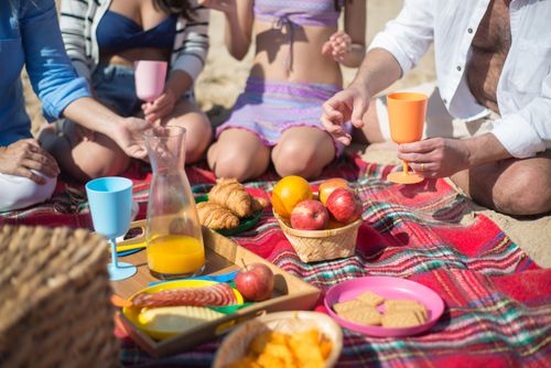 Free Enjoying a sunny beach picnic with friends, featuring fresh fruits, snacks, and drinks. Stock Photo