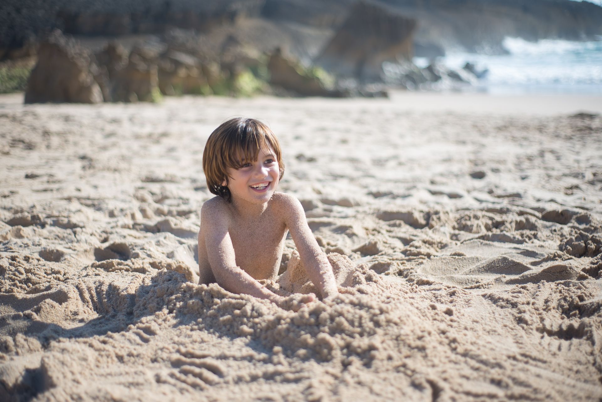 Child sitting in the sand at the beach, smiling