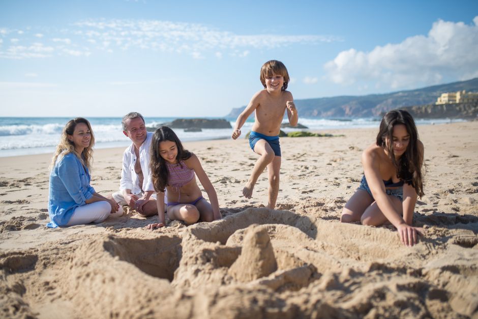 Família feliz construindo castelo de areia em praia paradisíaca, ideal para viagens de luxo com crianças.