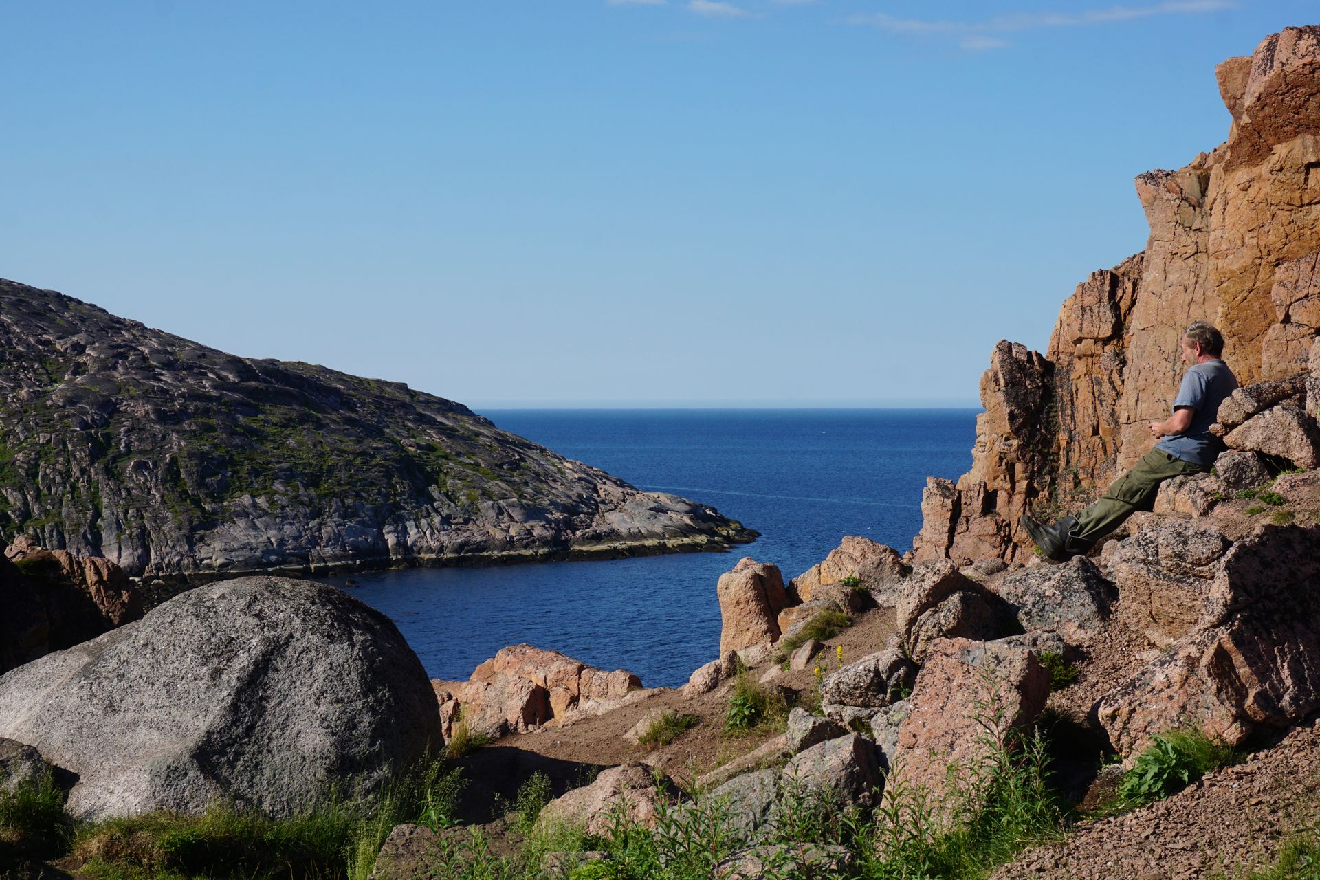 Man enjoys rugged coastal landscape at Murmansk Oblast, Russia, with rocky formations and blue sea.