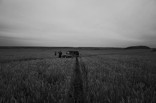 Grayscale Photography of People Standing on a Parked Car in the Middle of a Farm Field