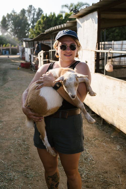 A Woman Carrying a Goat while Looking at the Camera