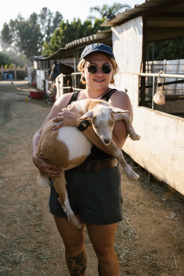 A Woman Carrying A Goat While Looking At The Camera