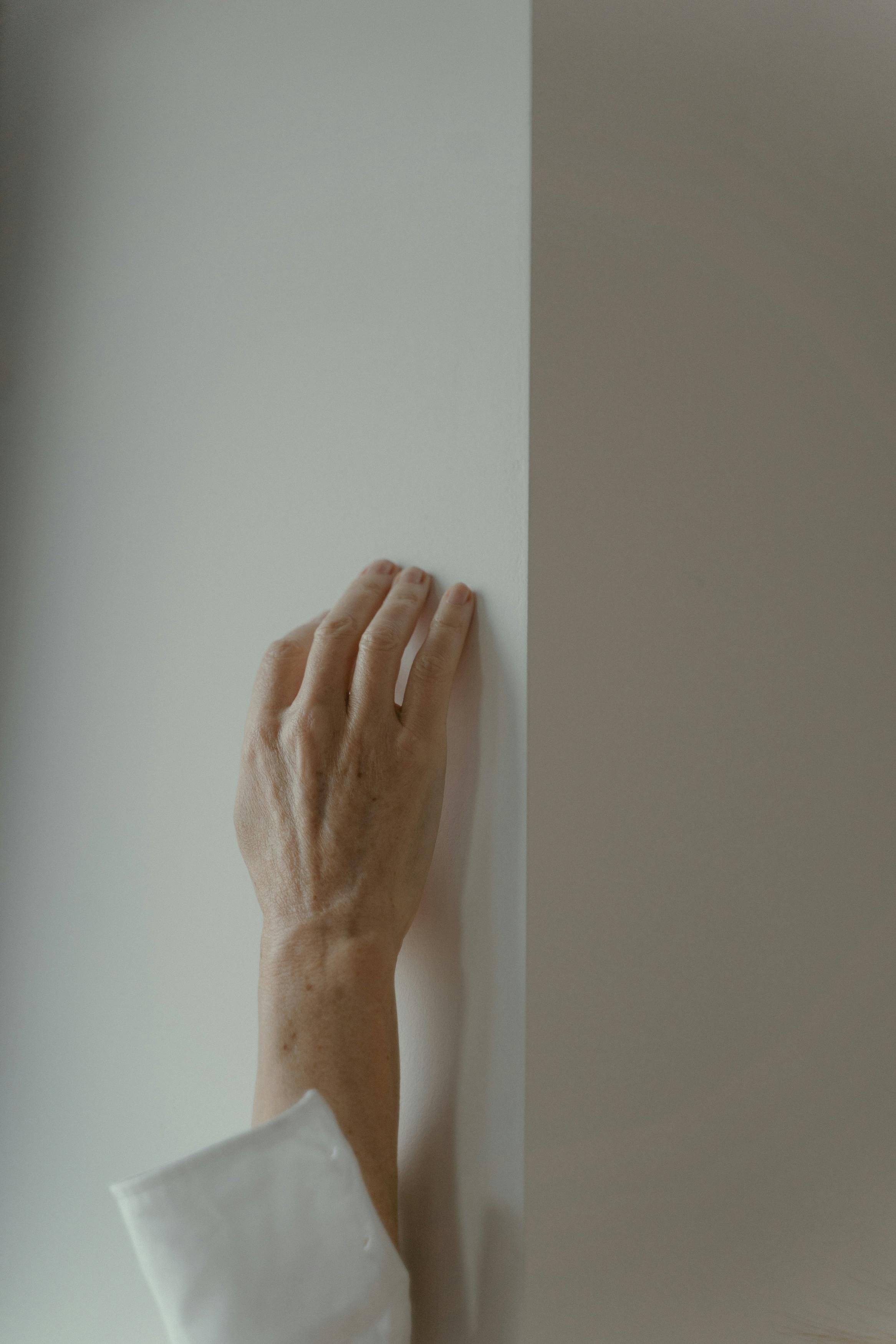 A close-up of a person's hand delicately touching a smooth white vertical wall.