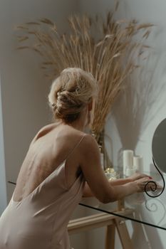 Graceful woman in sleepwear leans on glass table with candles, creating a serene indoor ambiance.
