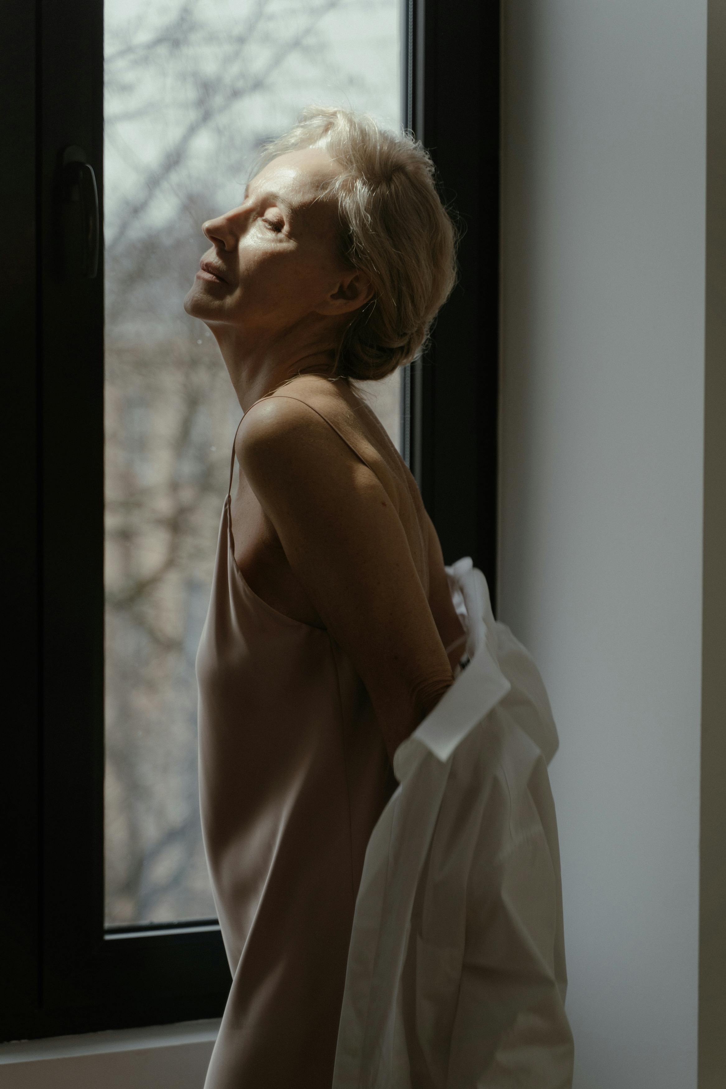 an elderly woman standing beside the window