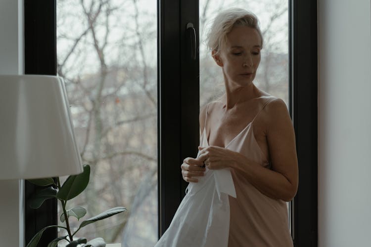 A Mature Woman Wearing Lingerie Standing Near Glass Window