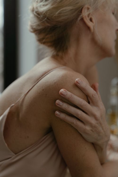 Free A senior woman's hand gently touching her shoulder, symbolizing care and tenderness. Stock Photo