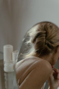 A blonde woman reflects in a round mirror, surrounded by candles, exuding tranquility.