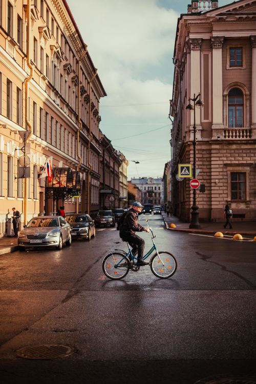 Free Man cycling across a European city street surrounded by classic architecture and parked cars. Stock Photo