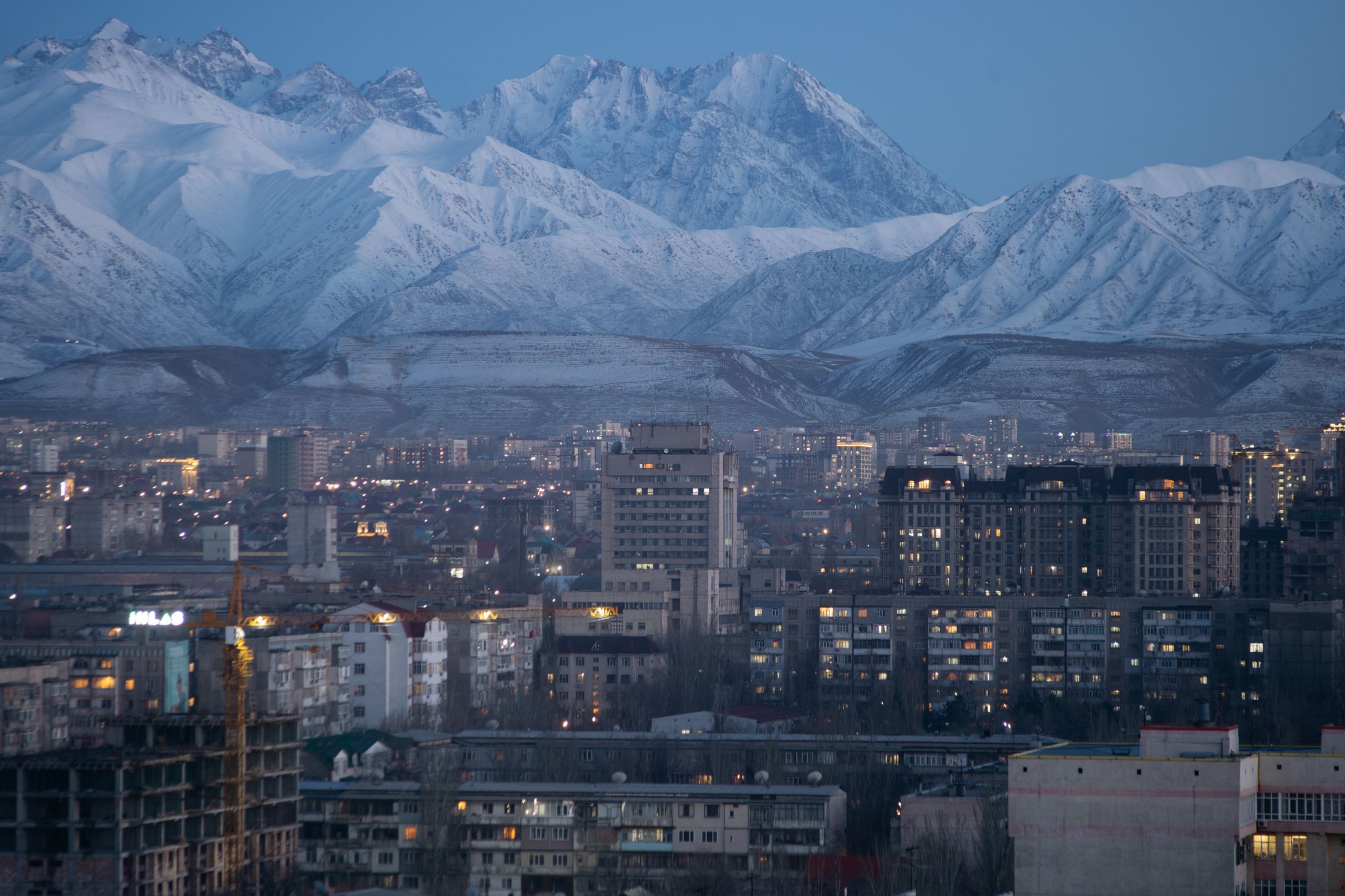 Photo by Arseniy Kotov Aerial twilight view of Bishkek city against snow-covered Tian Shan mountains, Kyrgyzstan