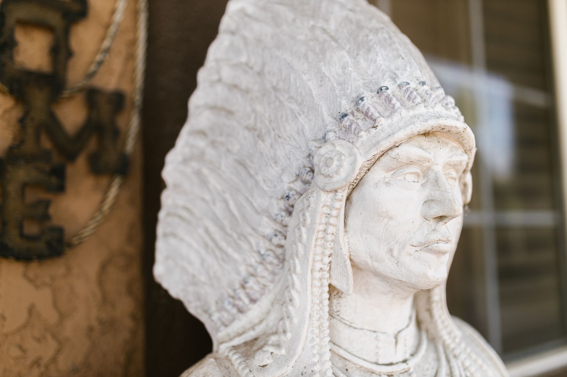 A detailed close-up photo of a stone sculpture depicting a Native American chief with a feathered headdress.
