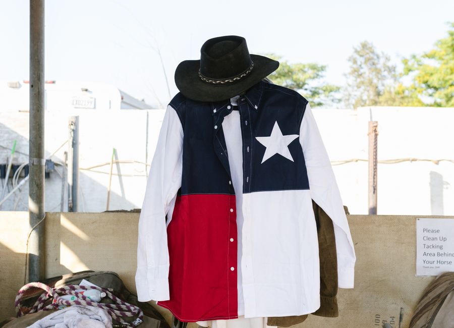 A Texas flag shirt and cowboy hat hanging outside. Represents Western fashion and lifestyle.