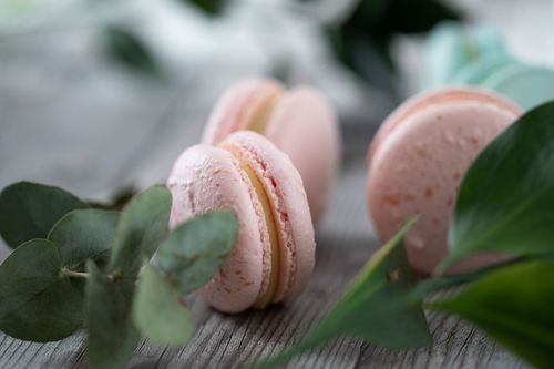 Free A close-up of pink macarons with green leaves on a rustic wooden surface, offering a charming dessert setting. Stock Photo