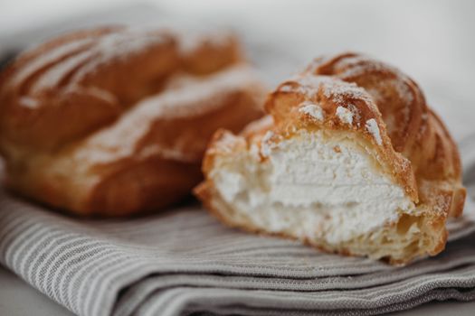 Close-up of a delicious cream-filled eclair dusted with powdered sugar on a striped cloth.