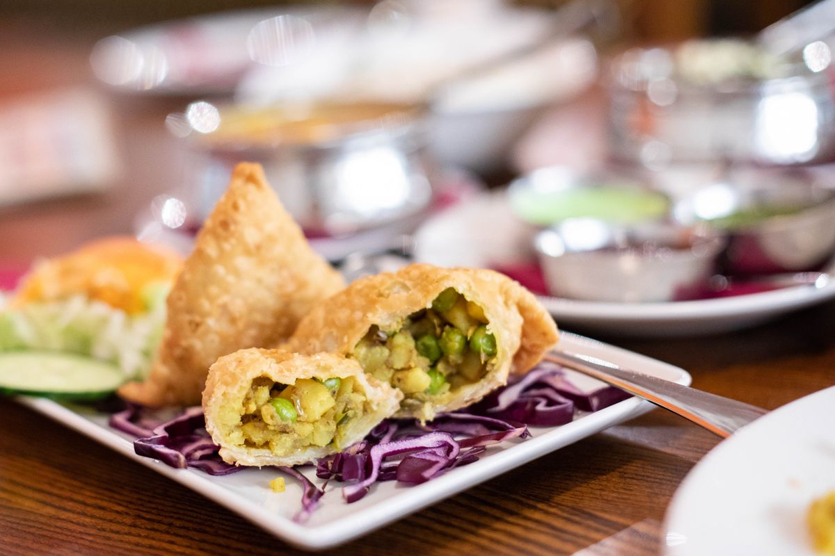 Crisp samosas, one broken open to show potato and green pea filling, on red cabbage