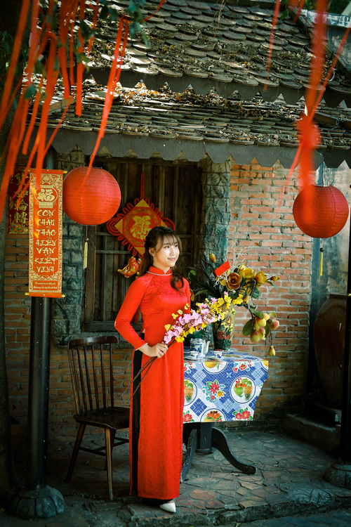 Free Asian woman in a red dress holding flowers in a vibrant traditional setting with red lanterns. Stock Photo
