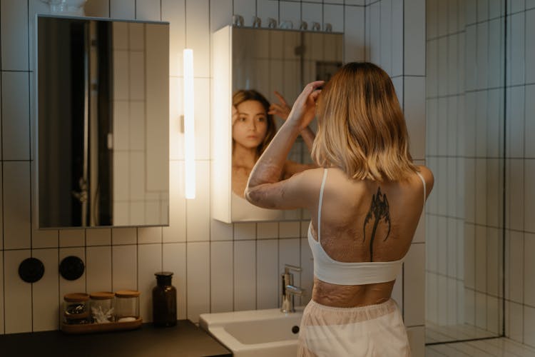 

A Tattooed Woman With Burn Scars Looking At A Mirror