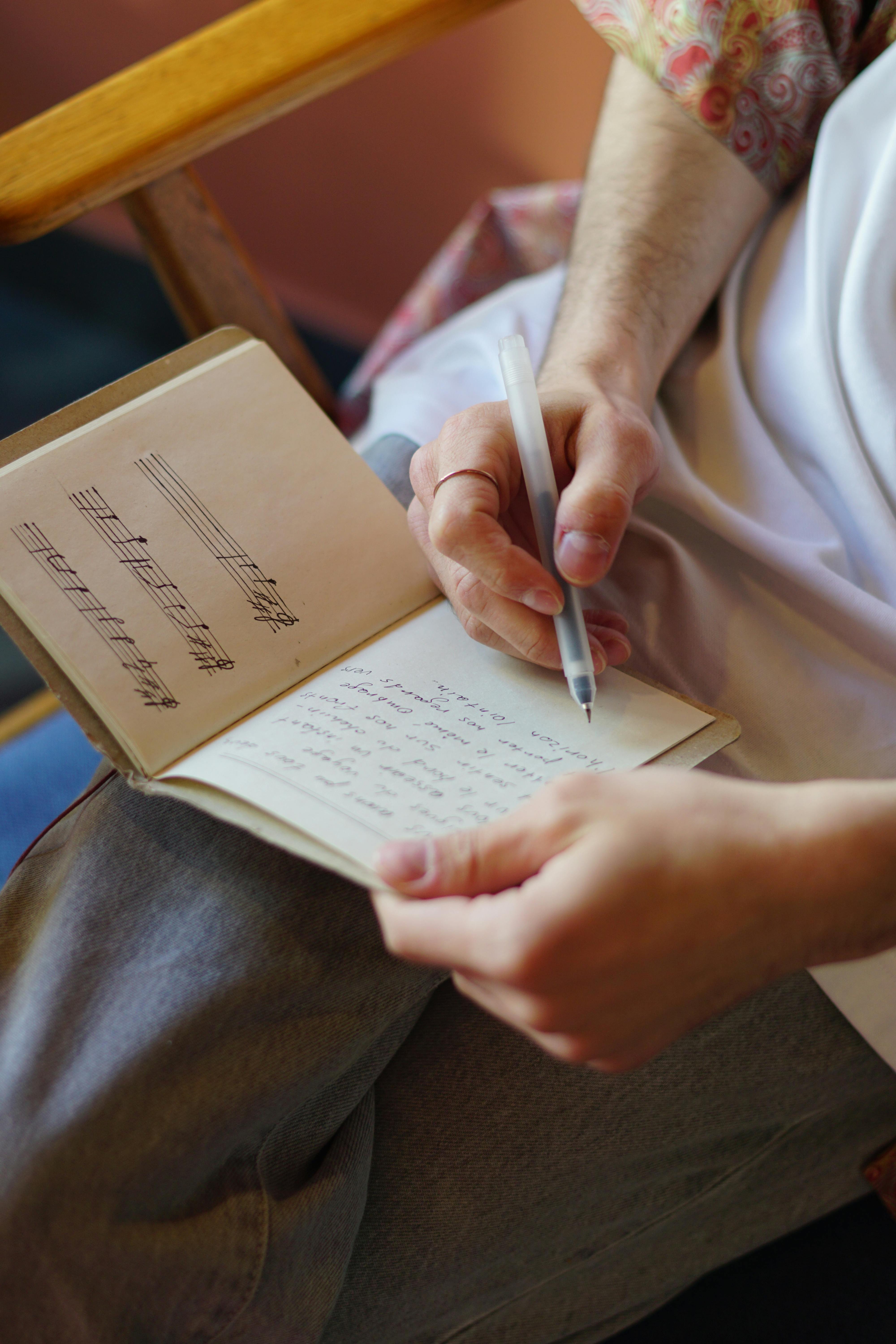 A man writing in a notebook with visible music scores, focusing on creativity and songwriting.