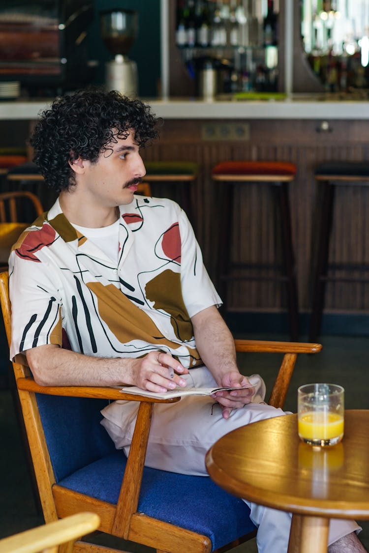 A Man Sitting On A Chair In A Café 