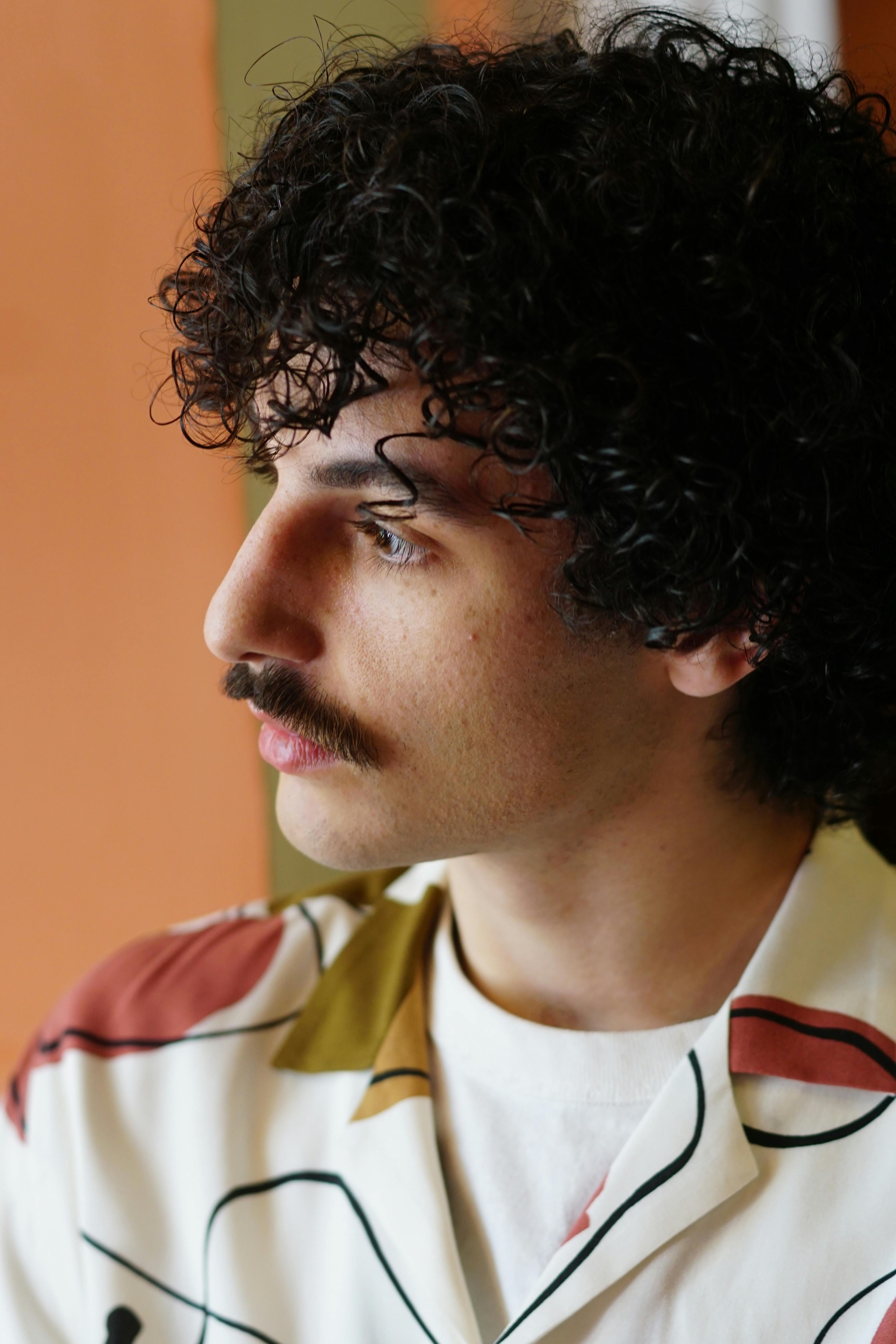 Side profile of a man with curly hair and mustache in a stylish patterned shirt.