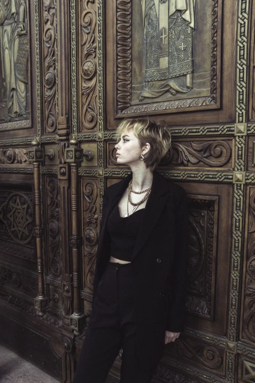 Free A fashionable woman in black standing by a decorative wooden door, exuding elegance and mystery. Stock Photo