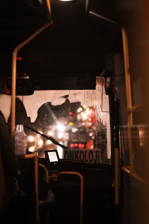 Free Interior view of a bus at night with raindrops on the window and blurred car lights visible ahead. Stock Photo